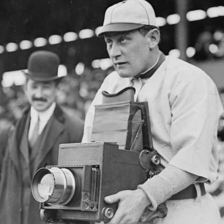 Afbeelding rechtenvrij: https://commons.wikimedia.org/wiki/File:5x7_Press_Graflex_camera,_produced_by_the_Folmer_%26_Schwing_Division_of_Eastman_Kodak_Co._held_by_Germany_Schaefer,_Washington_Senators_April_1911_LOC_2162646403_%28cropped%29.jpg